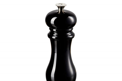 Le Creuset pepper mill on a dining table with peppers ready for seasoning.