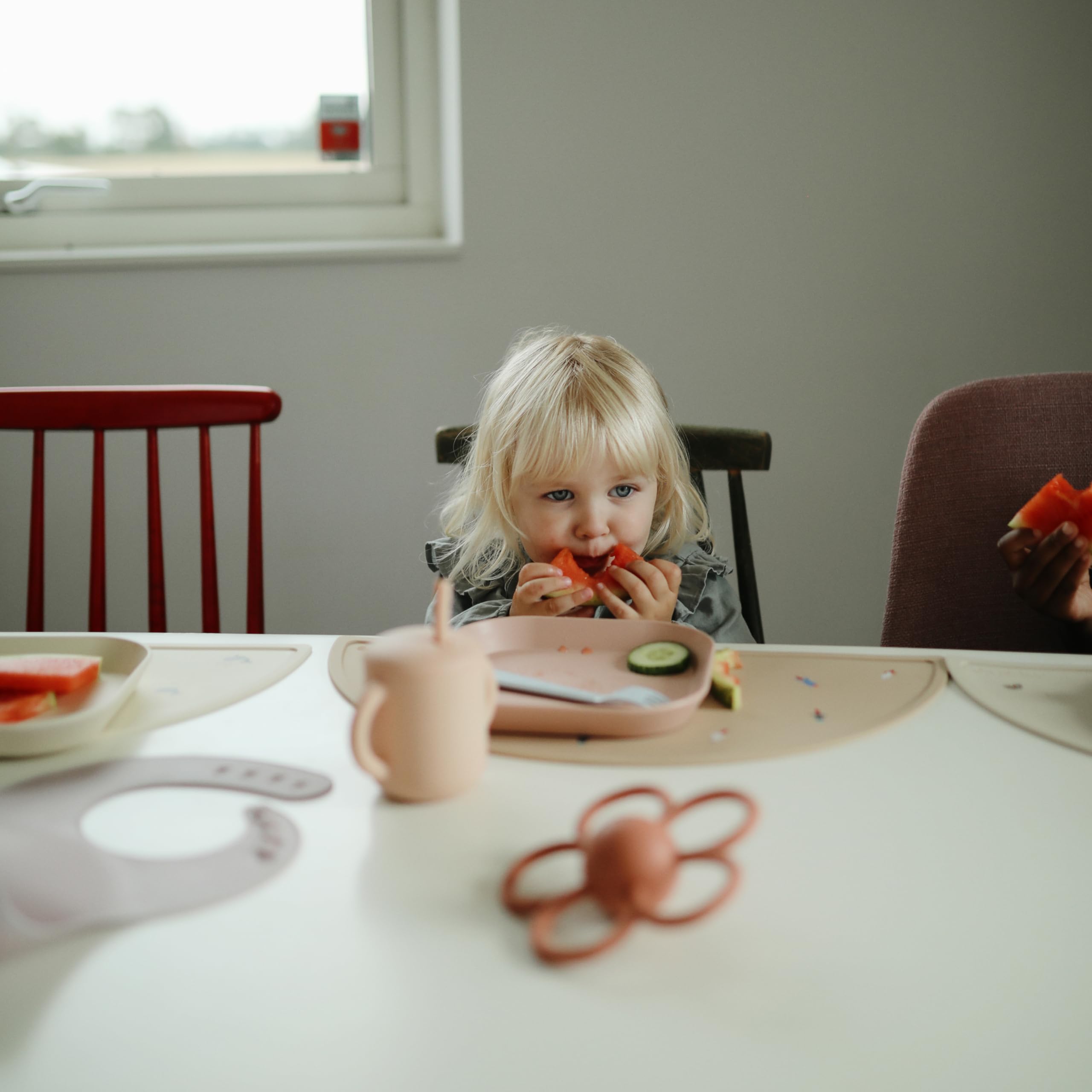 Travel-ready Mushie plates in blush, compact for on-the-go dining.