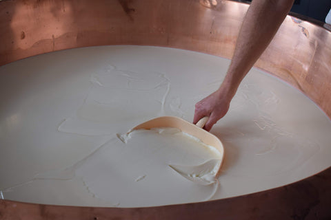 Pouring rennet solution into warmed milk for consistency.